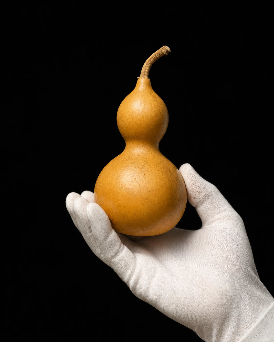 A golden hulu gourd held in a white-gloved hand